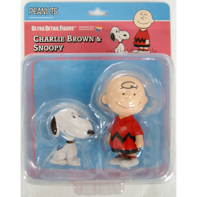 A collectible figure set featuring Charlie Brown and Snoopy from the Peanuts series. Charlie Brown is wearing a red short-sleeved shirt with a black zigzag stripe, black shorts, and white sneakers with black laces. He has his signature simple smile and a single curl of hair on his forehead. Snoopy, the white beagle with black ears, sits beside him wearing a black collar, gazing up with his usual friendly expression.