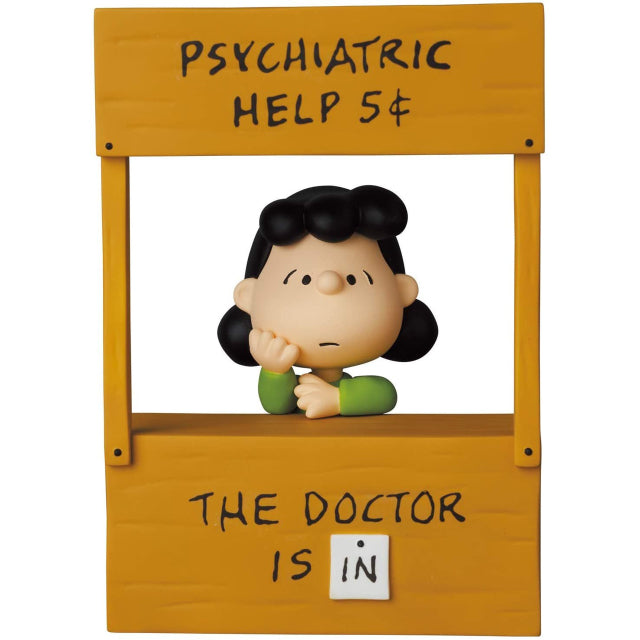 A collectible figure of Lucy Van Pelt from Peanuts, sitting behind her iconic 'Psychiatric Help 5¢' booth. The wooden stand features the words 'The Doctor is IN' on the front, while Lucy rests her chin on her hand with a thoughtful expression. This Medicom Ultra Detail Figure (UDF) captures the classic comic strip moment in detailed sculpting and vibrant colours.