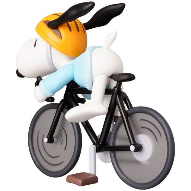 A detailed figure of Snoopy from the Peanuts series, riding a black road bicycle while wearing a light blue cycling outfit and an orange helmet. His ears are flapping back as he leans forward gripping the handlebars, giving a sense of speed and motion. The wheels of the bike have a stylized design, and the overall figure has a dynamic and playful look.