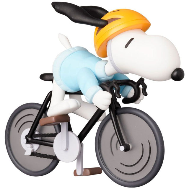 A detailed figure of Snoopy from the Peanuts series, riding a black road bicycle while wearing a light blue cycling outfit and an orange helmet. His ears are flapping back as he leans forward gripping the handlebars, giving a sense of speed and motion. The wheels of the bike have a stylized design, and the overall figure has a dynamic and playful look.